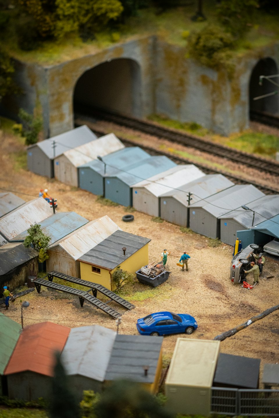 Miniaturfiguren arbeiten an einem umgedrehten Auto neben Bahngleisen und Garagen.