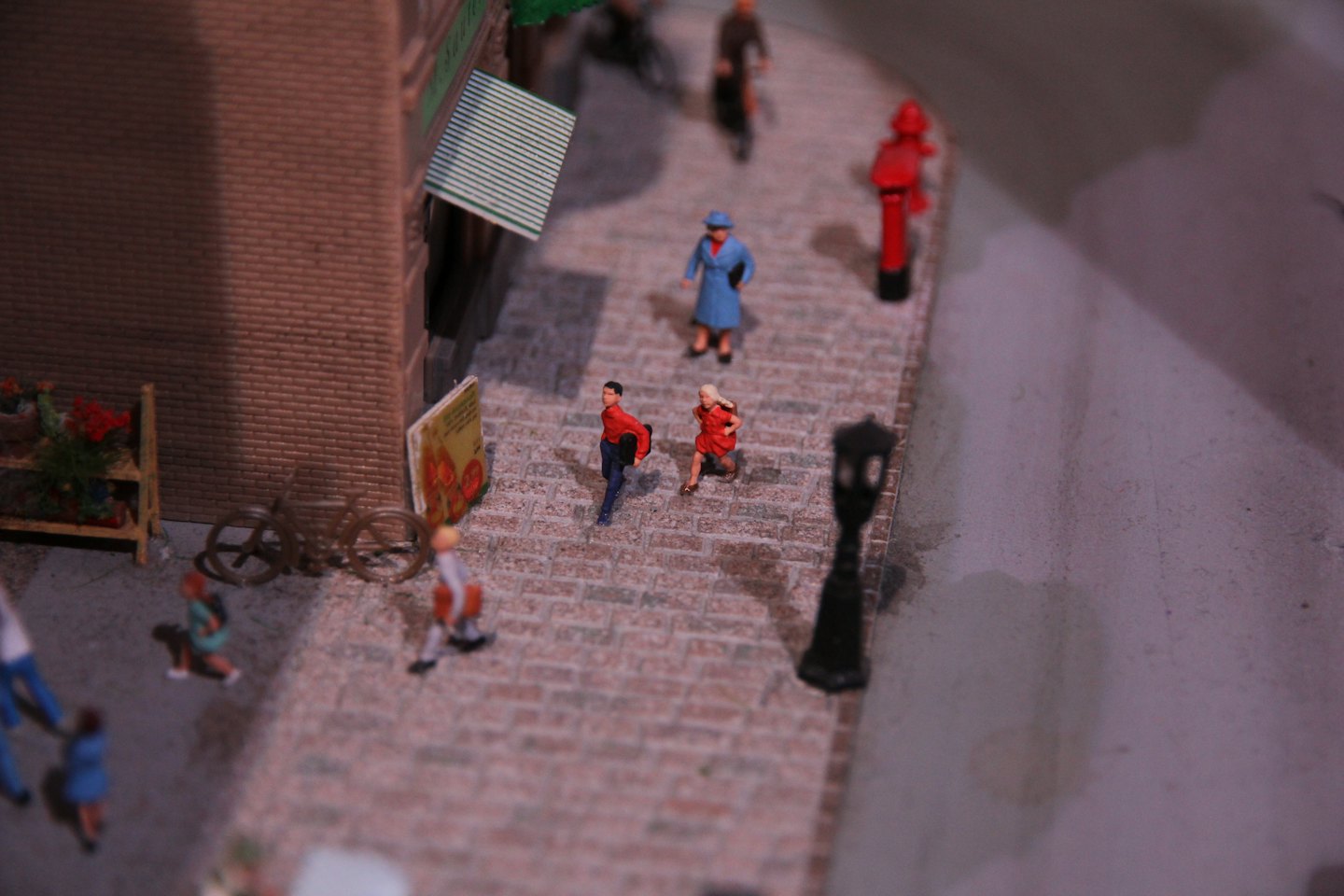 Winzige Figuren gehen auf einer Kopfsteinpflasterstraße in einer Miniatur-Diorama.
