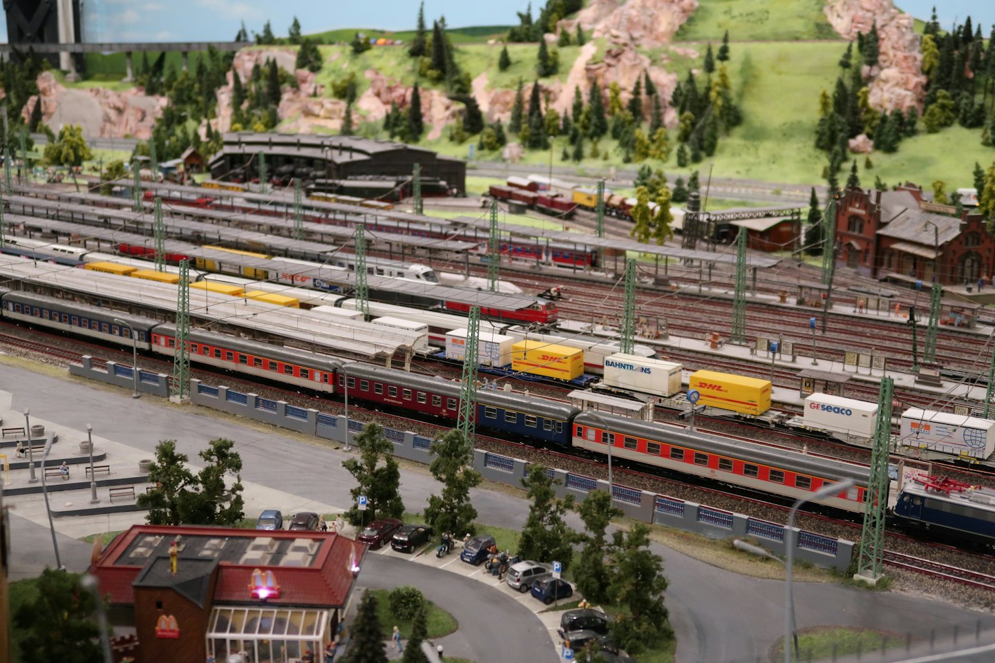 Detaillierte Modelleisenbahnanlage mit belebtem Bahnhof und Landschaft.