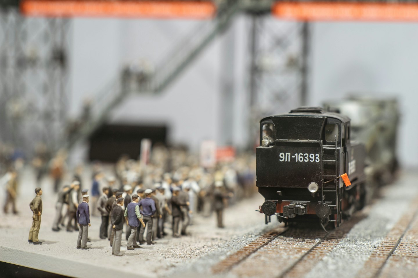 Kleine schwarze Lokomotive auf Gleisen mit winzigen Menschen drumherum.